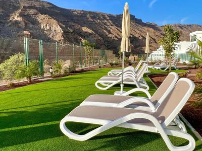 Chaises longues blanches avec coussins marron sur pelouse verte devant une vue de montagne ensoleillée.