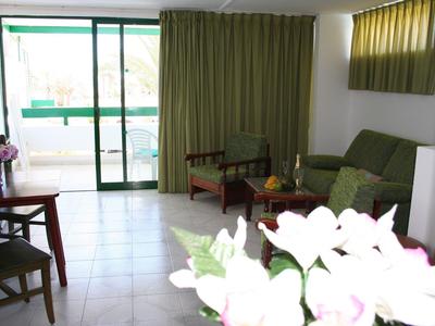 Helles Wohnzimmer mit grünen Vorhängen, Sofa, Stühlen, Holzmöbeln und weißen Blumen im Vordergrund.