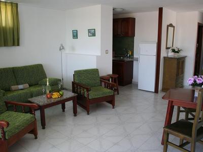 Helles Wohnzimmer mit grüner Sitzgruppe, Holzmöbeln und weißem Fliesenboden.