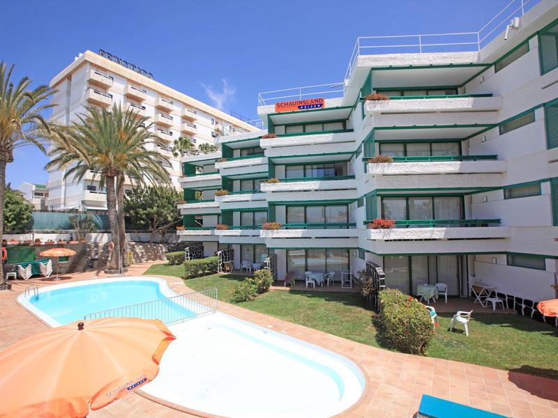 Complexe hôtelier avec piscine, chaises longues et palmiers sous un ciel dégagé
