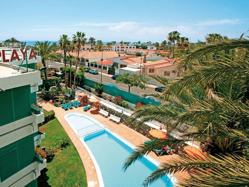 Vue sur une piscine d'hôtel entourée de chaises longues et de palmiers dans une station de vacances.