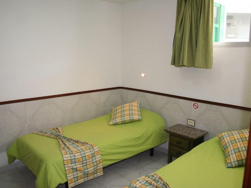 Petite chambre d'hôtel avec deux lits simples, couvertures vertes et une table de nuit entre eux.