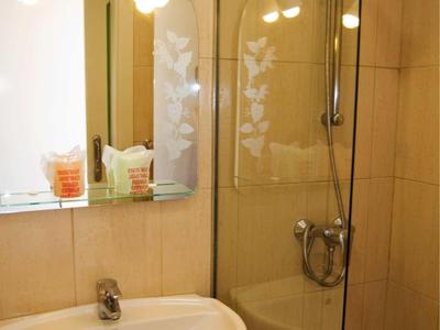 Kleines Badezimmer mit weißem Waschbecken, großem Spiegel und Dusche mit Glasabtrennung.