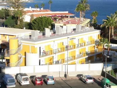 Mehrstöckiges gelb-weißes Gebäude mit Balkonen, Autos davor und Meer im Hintergrund sichtbar.