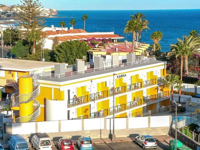 Edificio de hotel amarillo con balcones y vista al mar, rodeado de palmeras y coches.