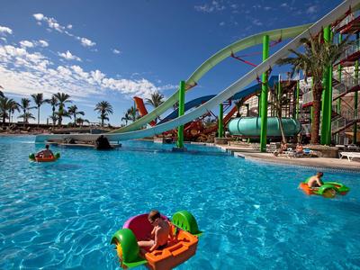 Toboggan aquatique coloré et enfants sur des bateaux dans une piscine d'un complexe tropical par une journée ensoleillée.