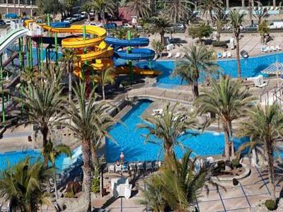 Grand complexe hôtelier avec plusieurs piscines, palmiers et parasols au bord de la mer.