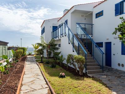 Weiße Ferienhäuser mit blauen Türen und einer Wegführung durch einen Garten zum Meer.