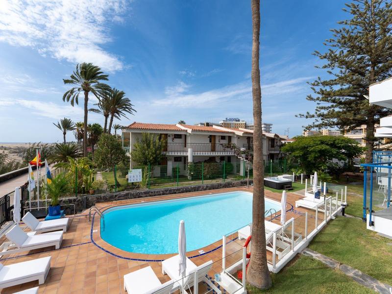 Piscina dell'hotel con lettini, palme e edificio su più piani sotto un cielo sereno