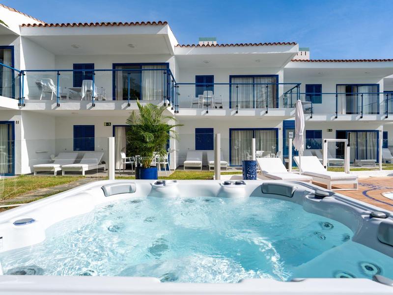 Complesso alberghiero moderno con vasca idromassaggio in primo piano e balconi con ringhiere in vetro.