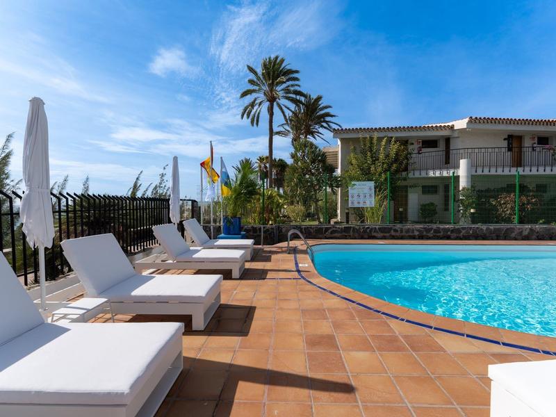 Comode sdraio accanto a una piscina con palme e cielo azzurro.