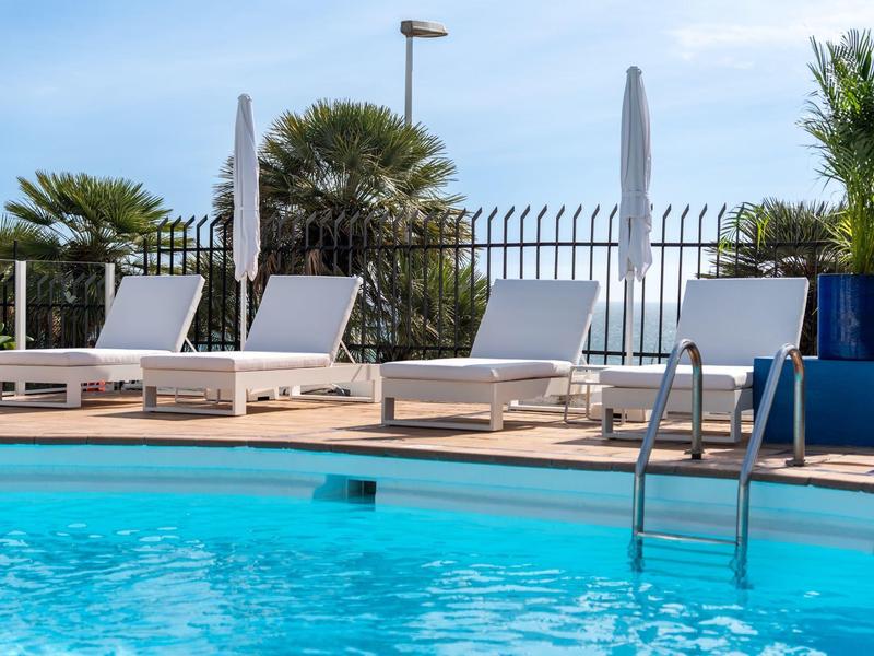 Area piscina con lettini e ombrelloni all'esterno di un hotel.