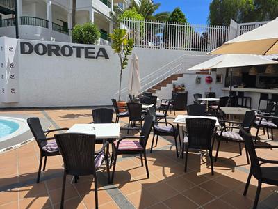 Hotel outdoor area with multiple tables and chairs beside a pool and a bar.