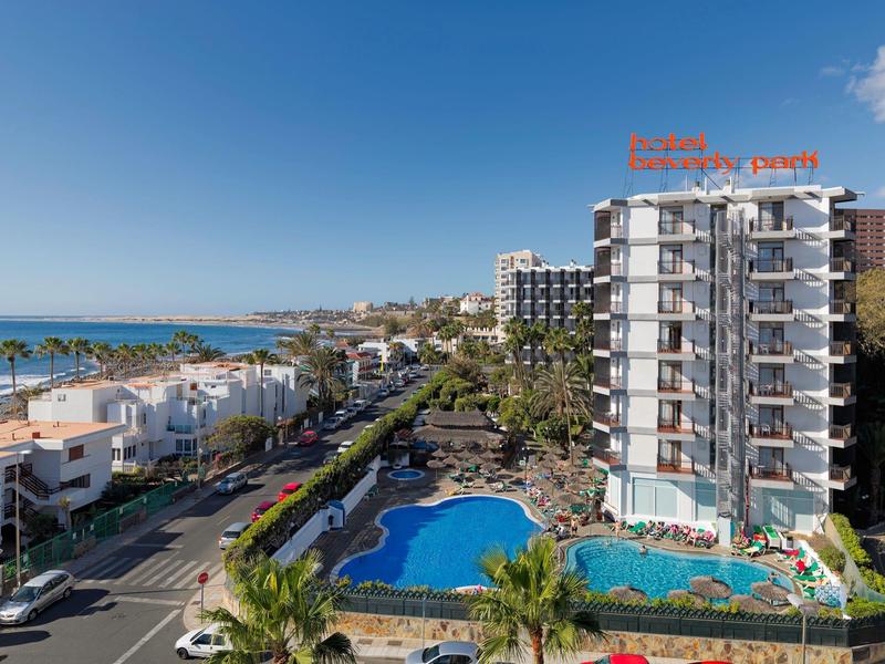 Vista de un hotel con piscinas, rodeado de palmeras y vista al mar en lugar turístico.