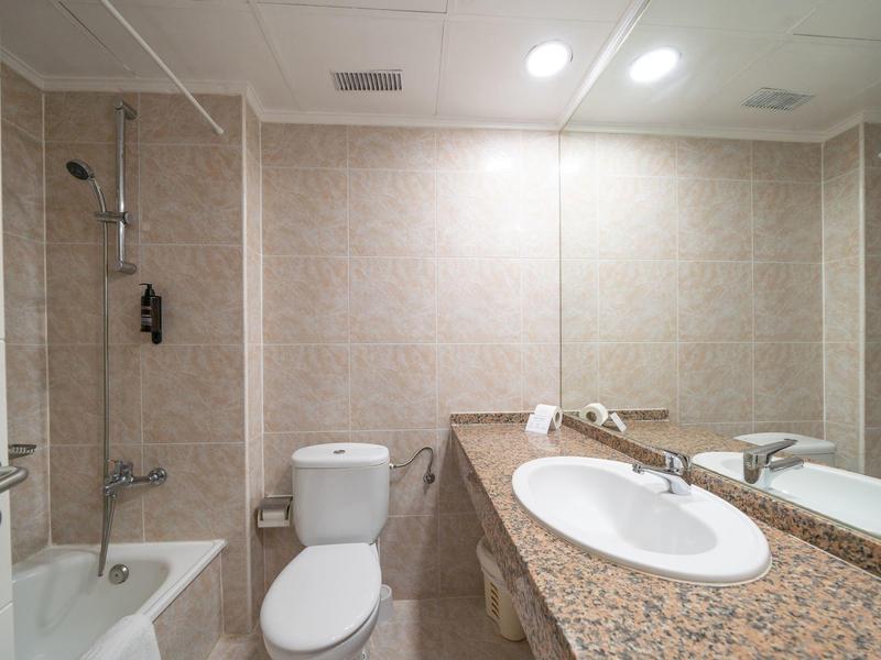 Baño pequeño con inodoro, bañera y lavabo con encimera de mármol y espejo grande.