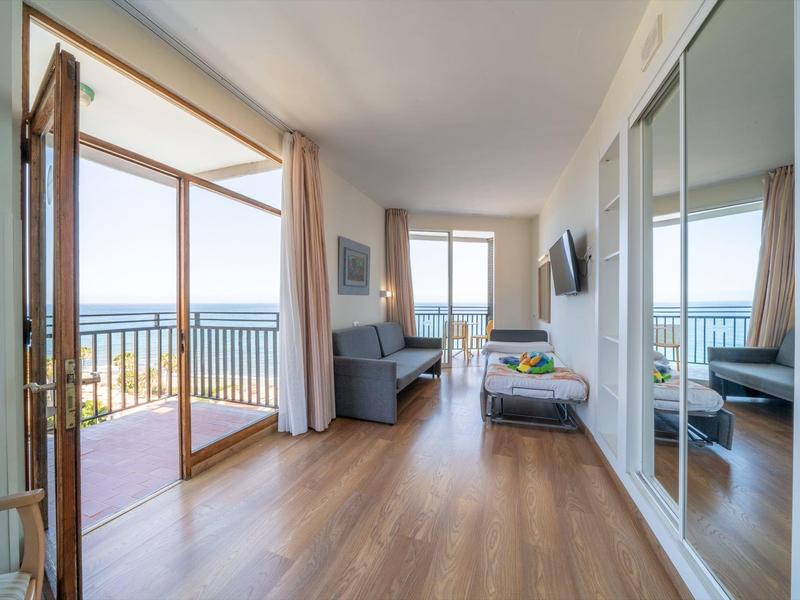 Habitación de hotel moderna con suelo de madera y vistas al mar a través de grandes ventanas y balcón.