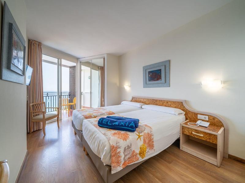 Habitación de hotel luminosa con cama doble, balcón contiguo y vista al mar.
