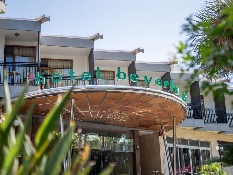 Entrada moderna del hotel con letrero verde y vegetación en primer plano.