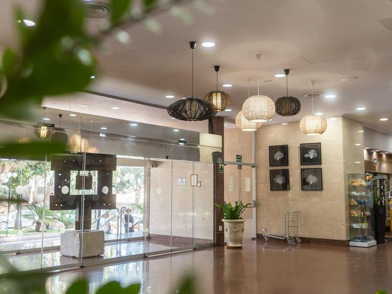 Área de recepción moderna de hotel con plantas, iluminación y asientos.