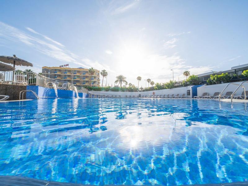 Gran piscina con agua azul clara en complejo hotelero con clima soleado.
