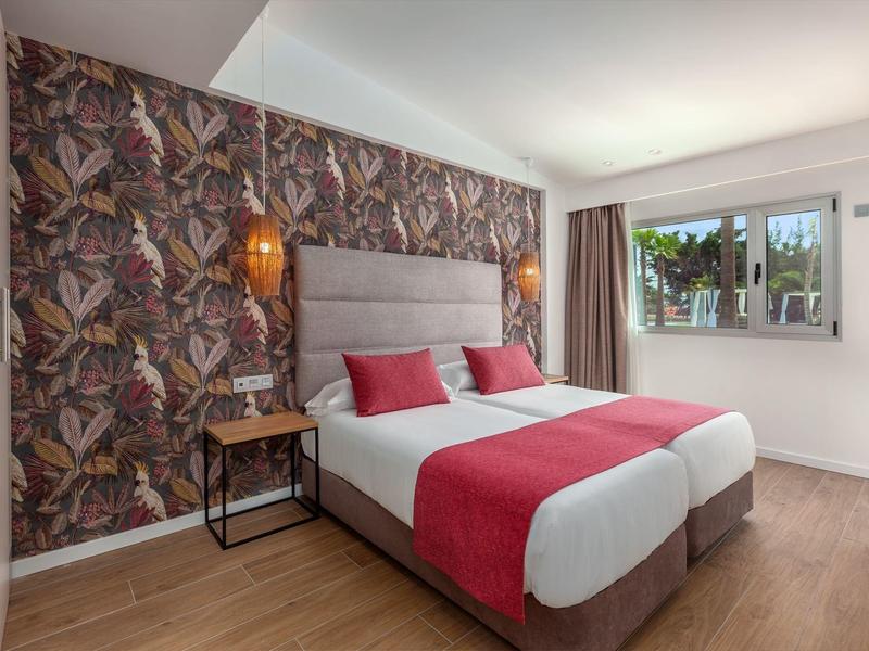 Modernes Schlafzimmer mit Doppelbett, roter Bettdecke, gemusterter Wand und Holzfußboden.