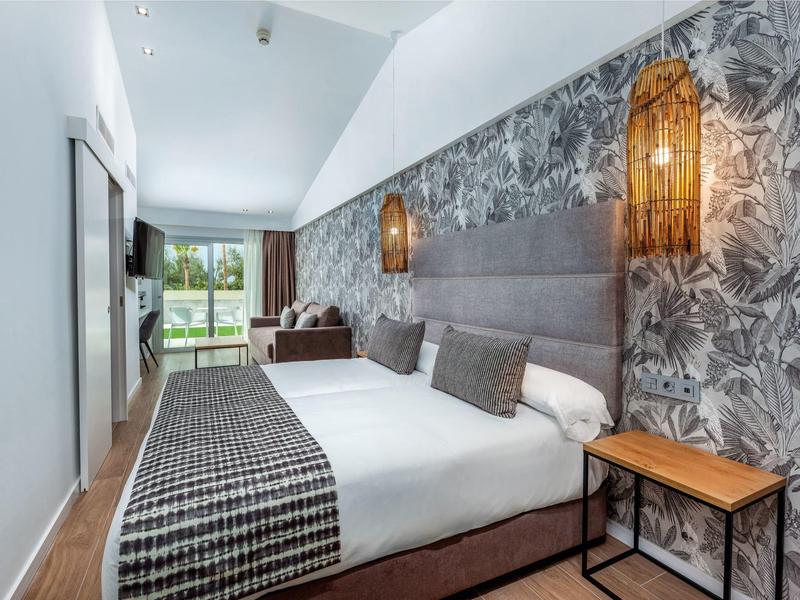 Modernes Schlafzimmer mit großem Bett, geflochtener Lampe, grauer Tapete und Balkon mit Aussicht.