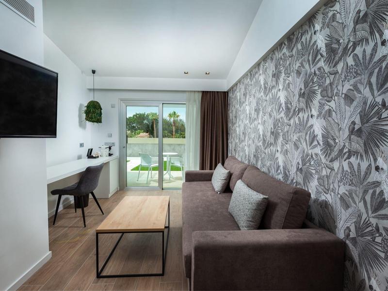 Modernes Wohnzimmer mit braunem Sofa, gemusterter Wand, Holztisch und Arbeitsplatz am Fenster.