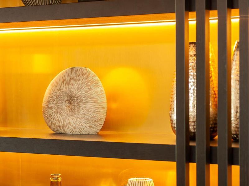 Regal mit orange-gelben Vasen und Steinskulptur vor goldglänzendem Hintergrund.