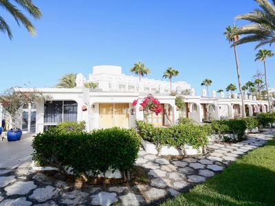 White hotel building with palm trees and shaded outdoor area under clear sky