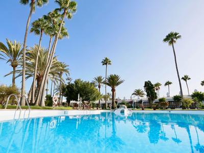 Klarer blauer Pool mit Palmen und blauem Himmel im Hintergrund.