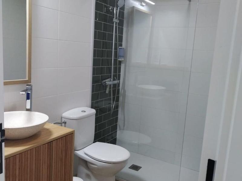 Moderne badkamer met douche, toilet, wastafel op houten kast en spiegel.