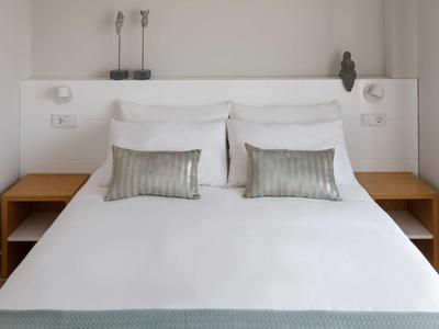 Dormitorio moderno con cama blanca, cojines grises y dos mesitas de noche de madera.