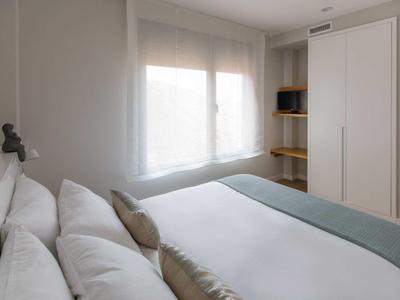 Habitación de hotel moderna y luminosa con cama doble, ventana con cortinas, TV y armario.