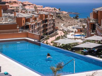 Piscina moderna con vista al mar en un complejo vacacional con casas en terraza y sombrillas.