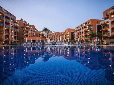 Modern hotel complex with large swimming pool and terraces at sunset.