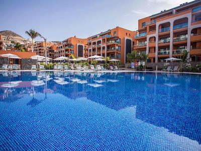 Large outdoor pool in front of a multi-story hotel with umbrellas and sun loungers