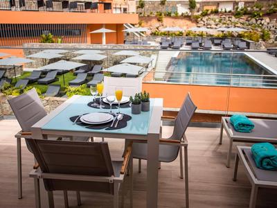 Mesa al aire libre con vajilla y bebidas junto a una piscina en un hotel moderno.