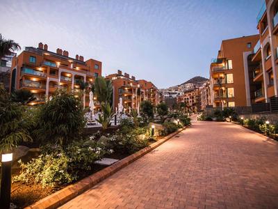 Camino pavimentado entre edificios de apartamentos iluminados al anochecer en un complejo turístico.