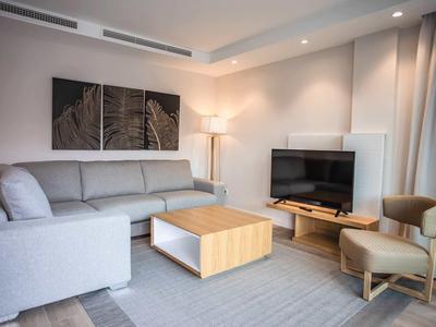 Sala moderna con sofá gris, mesa de madera, televisor y luces de acento en una habitación de hotel.