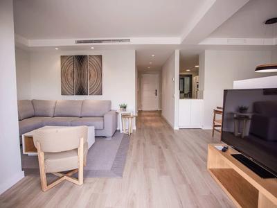 Sala luminosa con sofá gris, silla, televisor de pantalla plana y suelo claro de madera.