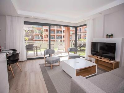Sala moderna con sofá, TV, sillón y acceso a una terraza con vistas a un jardín.