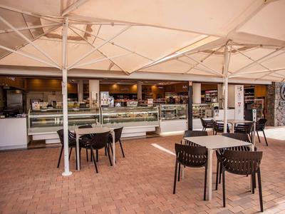 Zona exterior de una cafetería con mesas, sillas y terraza cubierta.