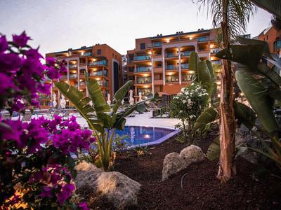 Hotel iluminado con piscina, rodeado de vegetación tropical al atardecer.