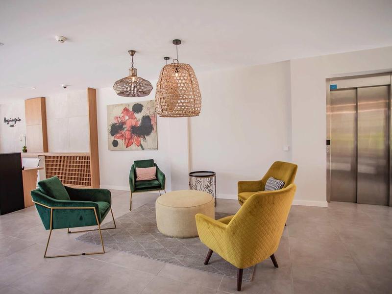 Área de salón moderno del hotel con sillones coloridos y ascensores al fondo.