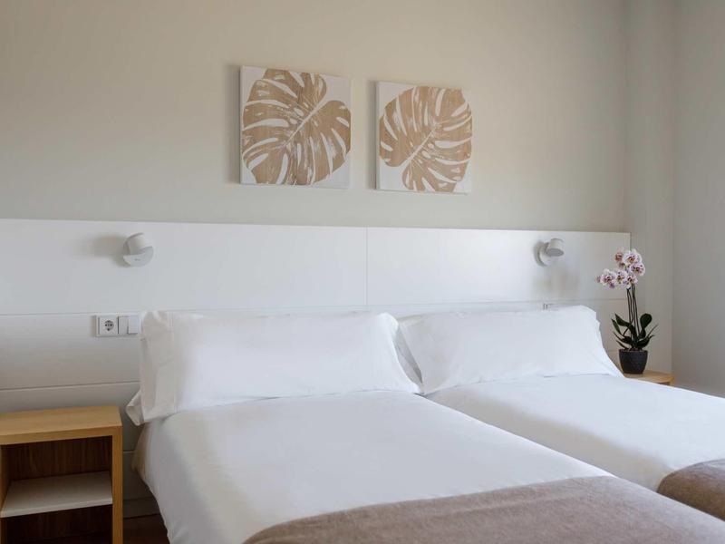 Piscina del hotel con tumbonas y sombrillas frente a un edificio de varios pisos con balcones.