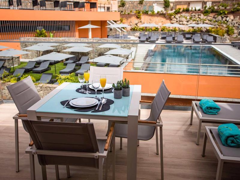 Mesa al aire libre con vajilla y bebidas junto a una piscina en un hotel moderno.