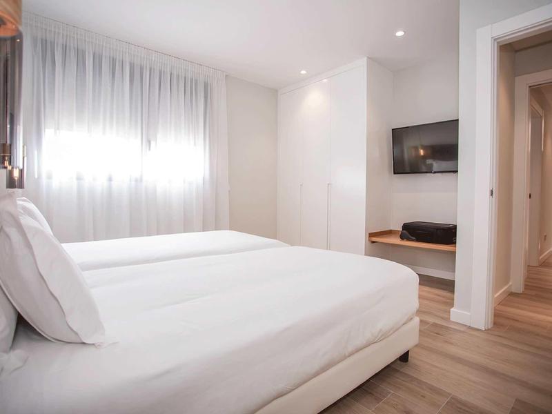 Habitación de hotel luminosa con dos camas, ropa de cama blanca y suelo de madera.