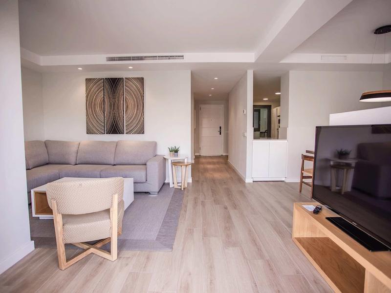 Sala luminosa con sofá gris, silla, televisor de pantalla plana y suelo claro de madera.