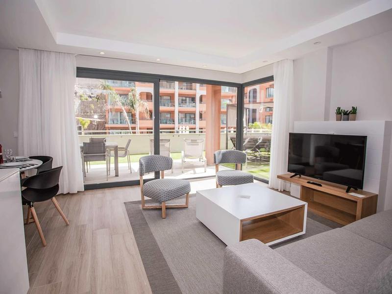 Sala moderna con sofá, TV, sillón y acceso a una terraza con vistas a un jardín.