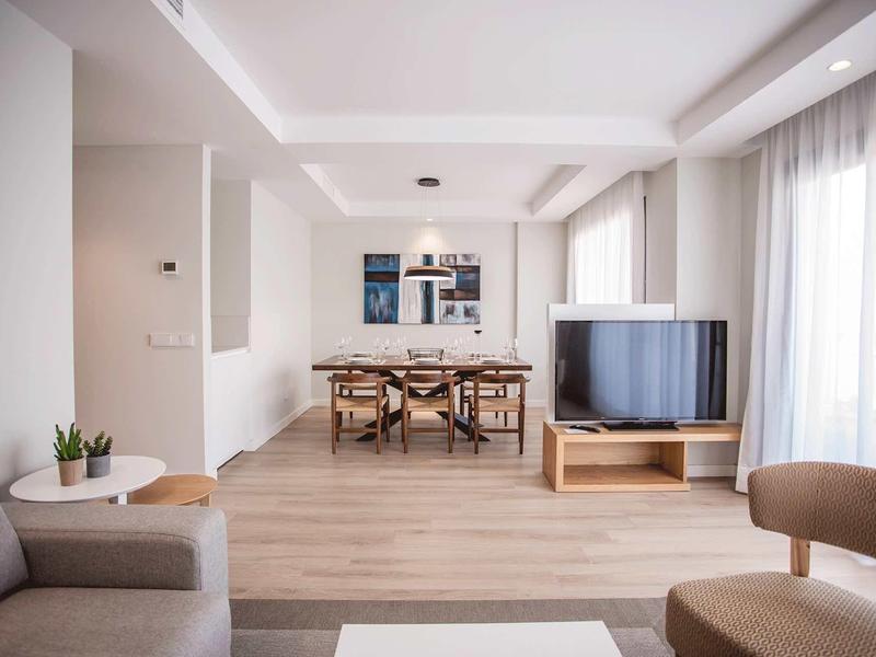 Área de estar y comedor moderna y luminosa con suelo de madera y ventana grande con cortinas.